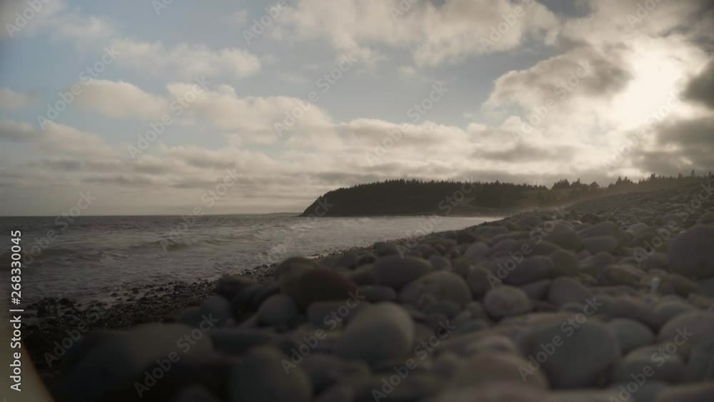 Ground shot of some waves hitting beach with some stones on the ground, trees and a road on the background near sunset in Halifax, Nova Scotia, Canada. Ground shot of some waves hitting beach with some stones on the ground, trees and a road on the background near sunset in Halifax, Nova Scotia, Canada.