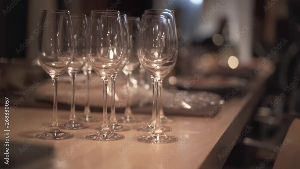 Close-up static shot of some empty clear wine glasses on a table ready for dinner along with some moddy lighting on a big dinning table. Close-up static shot of some empty clear wine glasses on a table ready for dinner along with some moddy lighting on a big dinning table.