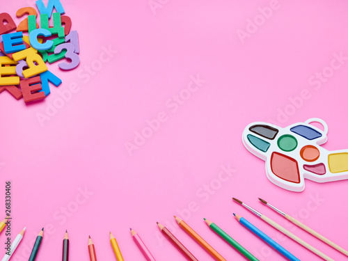 top view of the child's table, the composition of the paint brush letters numbers color pencils on a pink background