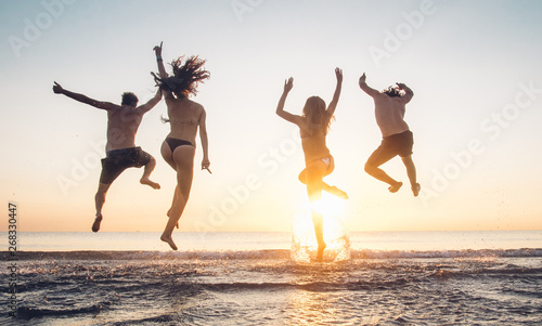 Group of best friends having fun jumping at the beach at sunset on vacation.