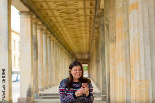 Latin lady interacts with her smartphone while standing in a passage