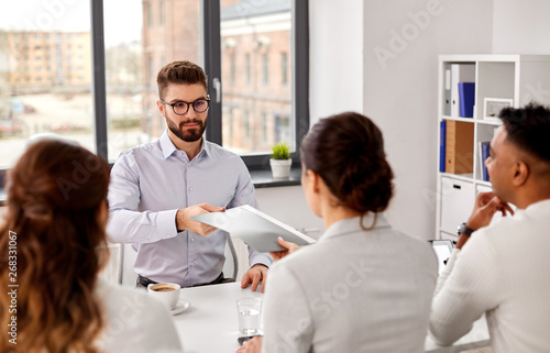new job, hiring and employment concept - male employee giving folder and having interview with team of recruiters at office