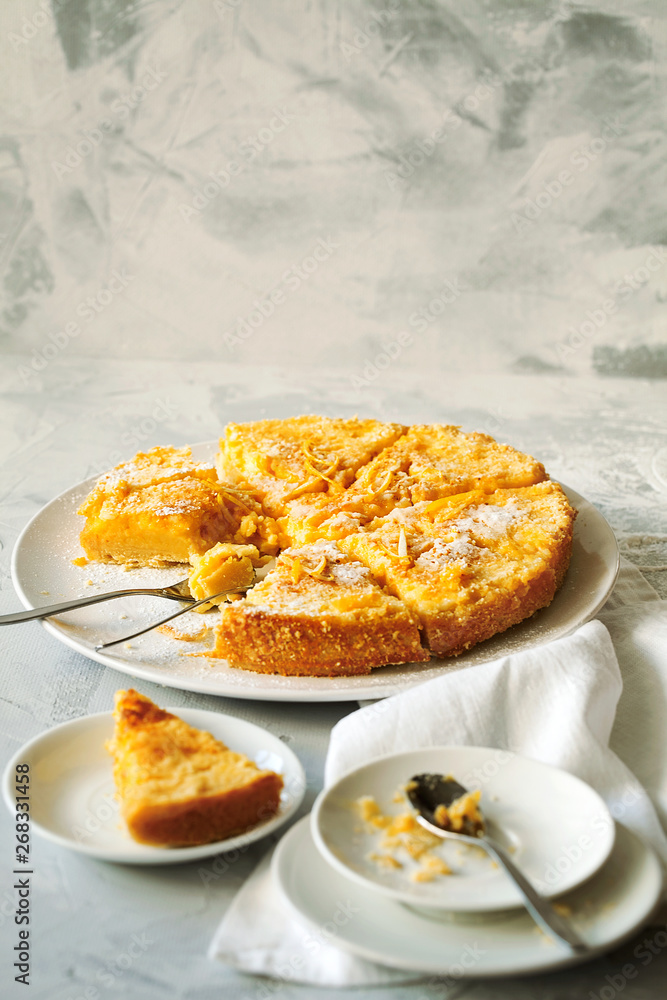 Traditional English lemon pudding cake with lemon twist and powdered sugar on a white plate on a light background with copy space for text.Homemade fruit pastries for the holiday table. Traditional English lemon pudding cake with lemon twist and powdered sugar on a white plate on a light background with copy space for text.Homemade fruit pastries for the holiday table.