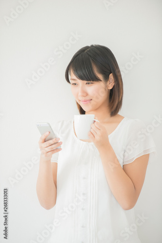 コーヒーカップを持ちスマートフォンを操作する女性