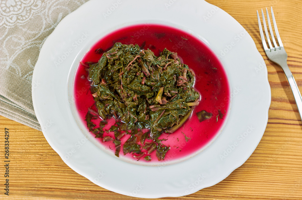 Prepaired braised amaranth - red spinach, in it's own juce on white plate on wooden table with linen textile and fork nearby, copy space, close up, top view, eco food and vegan eating concept. Prepaired braised amaranth - red spinach, in it's own juce on white plate on wooden table with linen textile and fork nearby, copy space, close up, top view, eco food and vegan eating concept.