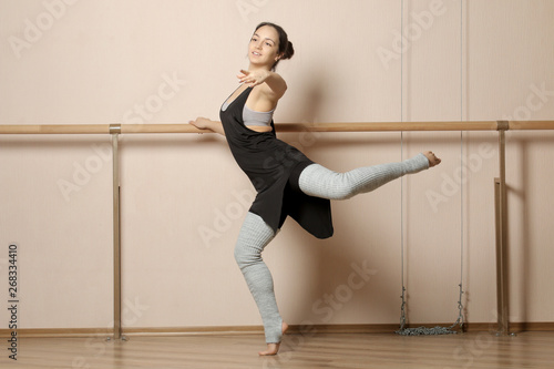 Beautiful girl dancer. The girl does exercises and various tricks near the ballet barre. Ballerina doing a sports workout in a dance studio near a ballet barre.