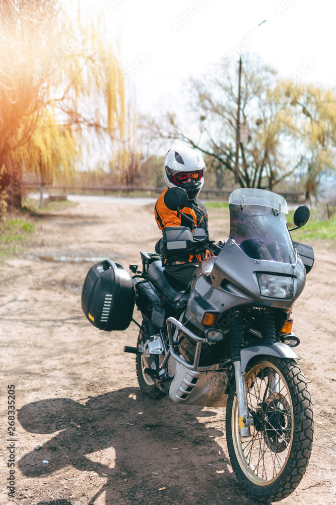 Obraz premium Biker girl wearing a motorcycle outfit, protective clothing, equipment, adventure touristic motorbike with side bags. outdoor travel, active traveler, vertical photo