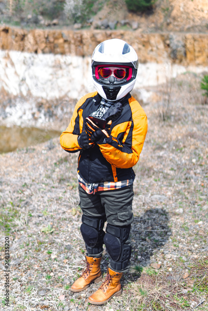 Biker girl wearing a motorcycle outfit, protective clothing, equipment, adventure tourist. outdoor travel, active traveler and red sunglasses. use smartphone Biker girl wearing a motorcycle outfit, protective clothing, equipment, adventure tourist. outdoor travel, active traveler and red sunglasses. use smartphone