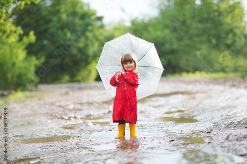 Happy child  with an umbrella playing out in the rain in the summer outdoors photo