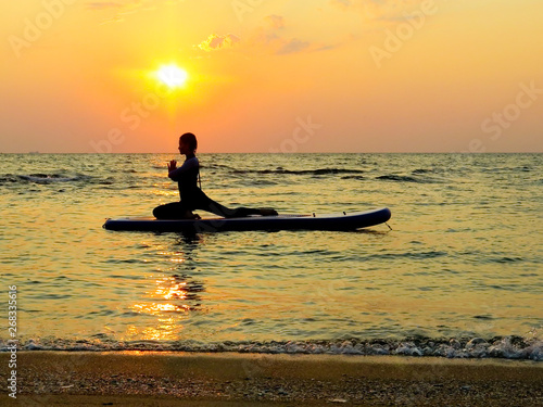 young happy girl woman doing yoga at sea on a SUP water board. Meditation. Beautiful dawn. Sport health holidays © agusyonok