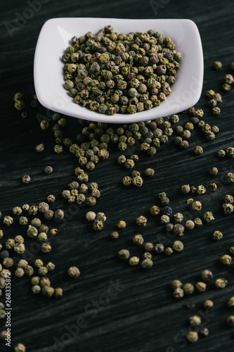 Green peppercorns in white bowl on wooden background