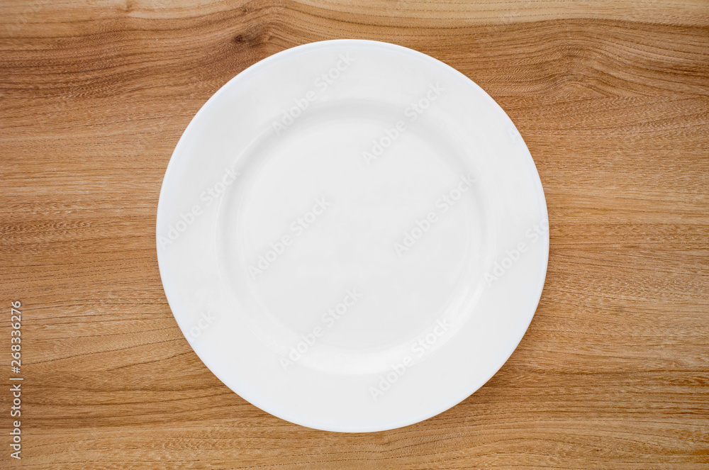 Round white plate on a wooden table. View from above Round white plate on a wooden table. View from above