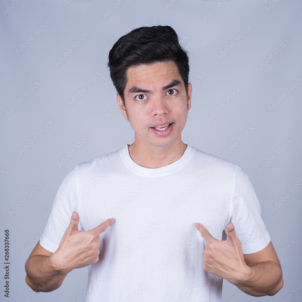 Portrait handsome young asian man wearing a white T-shirt pointing at himself asking you mean me isolated on grey background. Asian man people. business success concept. Portrait handsome young asian man wearing a white T-shirt pointing at himself asking you mean me isolated on grey background. Asian man people. business success concept.