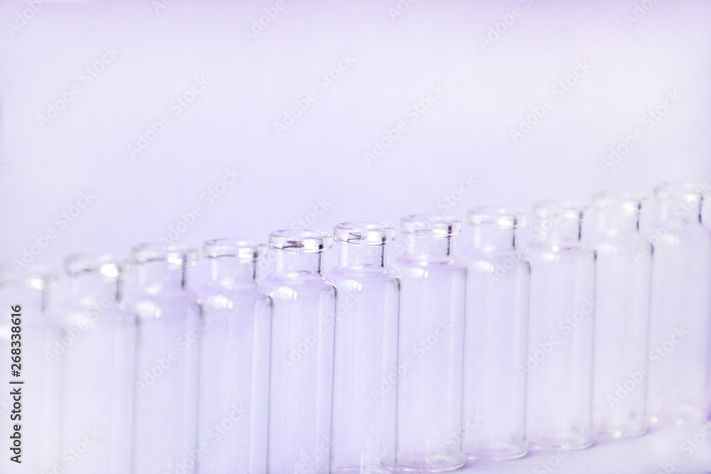 Empty glass medical vials, ampoules in a row on a light violet background with space for text. Glass medical bottles with selective focus. Vaccines, Medicine, Laboratory, Immunization concept. Empty glass medical vials, ampoules in a row on a light violet background with space for text. Glass medical bottles with selective focus. Vaccines, Medicine, Laboratory, Immunization concept.