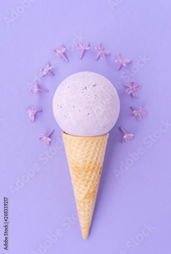 Composition of ice cream cone with bath ball on a violet background. Bathroom cosmetic accessories. Flat Lay. Top View. Lilac flowers