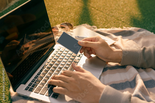 Hands holding credit card and using laptop on natural summer background