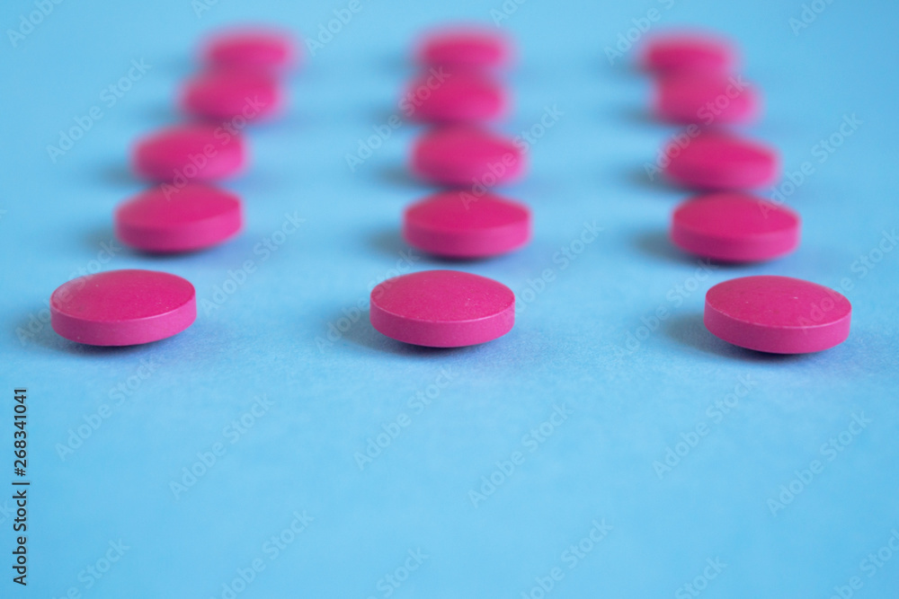 Pink pills in line on blue background. Close-up. Concept medicine, pharmacology Pink pills in line on blue background. Close-up. Concept medicine, pharmacology