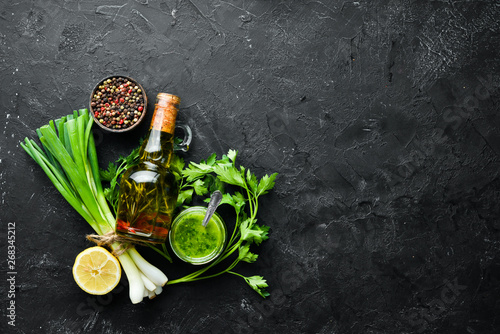 Ingredients for chimichurri sauce: fresh parsley, onion, garlic, olive oil, lemon. On a black background. Top view. free space for your text. photo