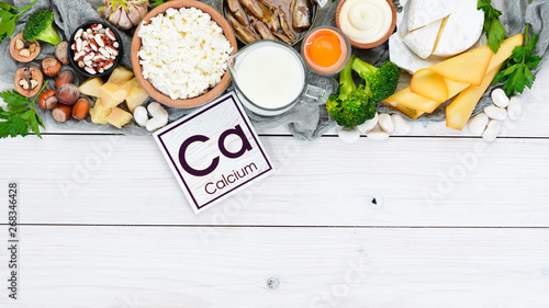 Food with calcium. A variety of foods rich in calcium: cheese, milk, parmesan, sour cream, fish, almonds, parsley, garlic, broccoli. On a white wooden background. Top view. Free copy space. photo