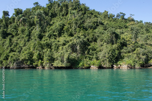 The sea is blue and have vegetation all around. The sky is blue with some clouds.  