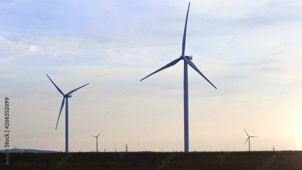 Evening silhouette of windmills with sun setting in background on a cloudy blue sky. These clean energy generating wind farms are densely populated in the state.
