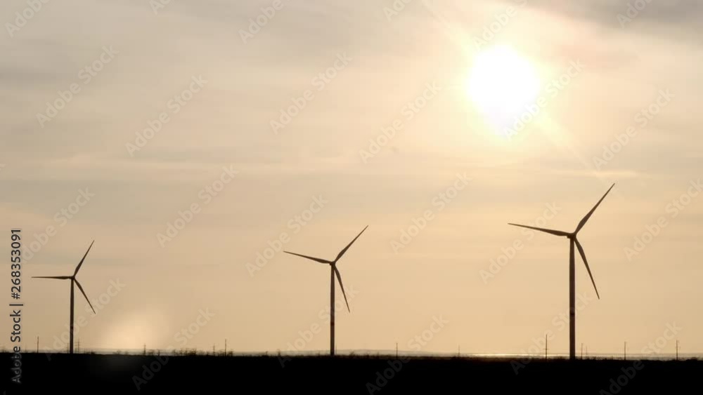 Evening silhouette of windmills with sun setting in background on a cloudy blue sky. These clean energy generating wind farms are densely populated in the state. Evening silhouette of windmills with sun setting in background on a cloudy blue sky. These clean energy generating wind farms are densely populated in the state.