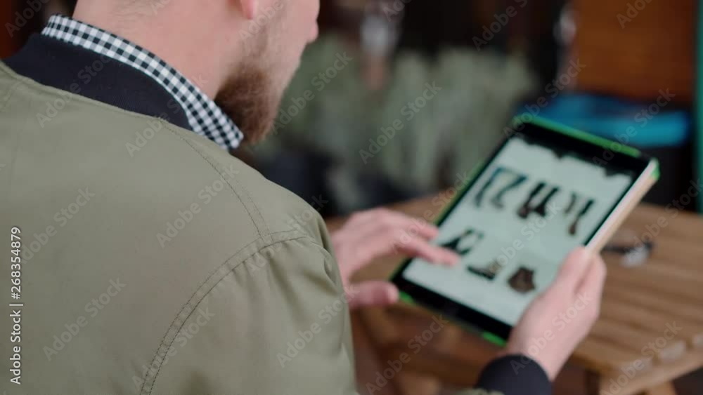 Bearded man is choosing shoes in online store by tablet, browsing site Bearded man is choosing shoes in online store by tablet, browsing site