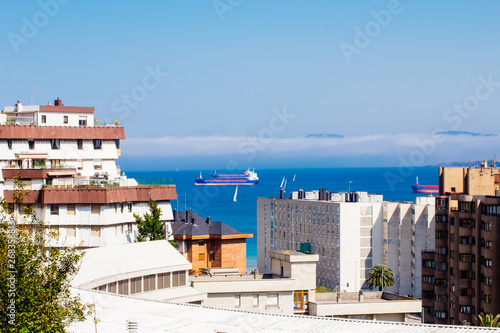 Cargo ships and sailing boats on the coast of the city of Santander, Cantabria, Spain. Thick sea mist in the background.