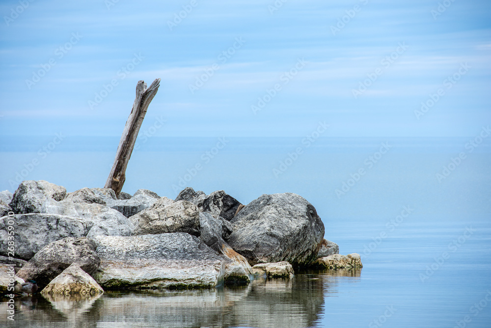 driftwood log in rocks on Lake Michigan coast with water reflection driftwood log in rocks on Lake Michigan coast with water reflection