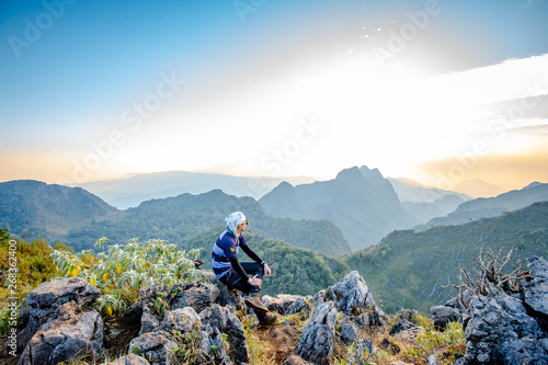 Man sitting back to clear sky Cloud wait for sunset at top of wildlife sanctuary name Doi Luang Chiang Dao, Thailand with Shadow of mountain layer and sun ray.