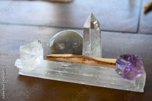 Assortment of healing crystals, clear quartz tower, selenite rod, palo santo, ametrine, and rough clear quartz chunk. Natural lighting, crystals on table outside in Puerto Rico. Reiki meditation. 