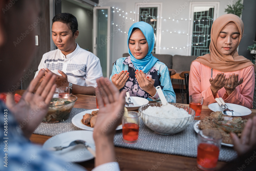 Hijab women and a man pray together before meals, a fast breaking meal served on a table in backyard