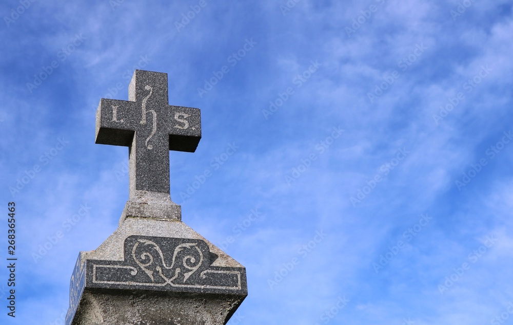 I.H.S. represtenting Jesus Christ on cross on top of old gravestone with wispy clouds in blue sky in background