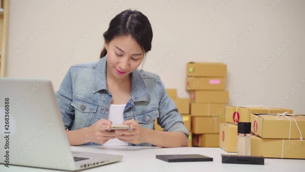 Smart Asian young entrepreneur business woman owner of SME online checking product on stock and save to mobile phone working at home. Small business owner at home office concept. Smart Asian young entrepreneur business woman owner of SME online checking product on stock and save to mobile phone working at home. Small business owner at home office concept.