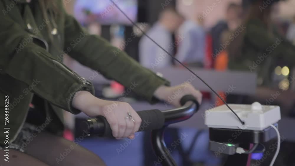 Young girl in virtual reality, rides a bicycle at the exhibition of computer technology. Beautiful young girl playing with vr glasses. Young girl in virtual reality, rides a bicycle at the exhibition of computer technology. Beautiful young girl playing with vr glasses.