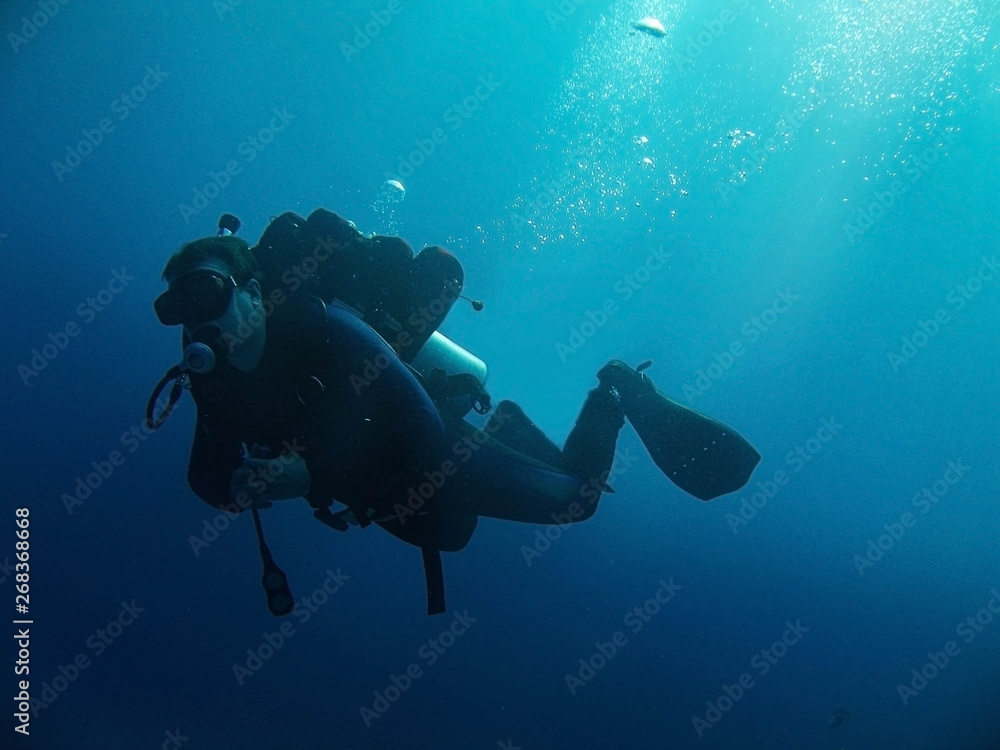 Scuba diver with full equipment is underwater. Sunlight and bubbles.  