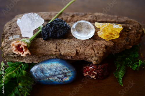 Variety of healing crystals on wooden table. Rose Quartz, Tektite, Labradorite, Brecciated Jasper, Amber, and Clear Quartz. Crystals of all shapes and sizes, natural lighting. Shiny witchy crystals.