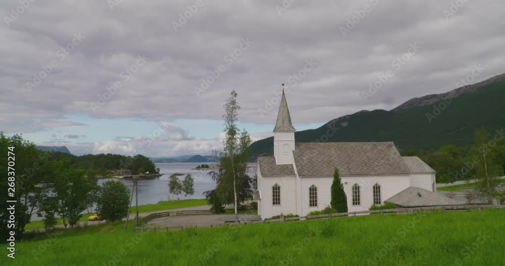 White wooden church at the end of a Norwegian fjord, on a hillside with grass White wooden church at the end of a Norwegian fjord, on a hillside with grass