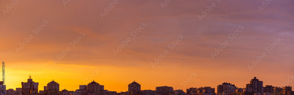 Modern city skyline. Dramatic orange sunset clouds over modern city rooftops wide panorama.