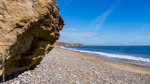 Rocky cliff face to the left of a pebble beach at Seaham Hall in County Durham, England.  North Sea to the right and blue skies in the background to the horizon.