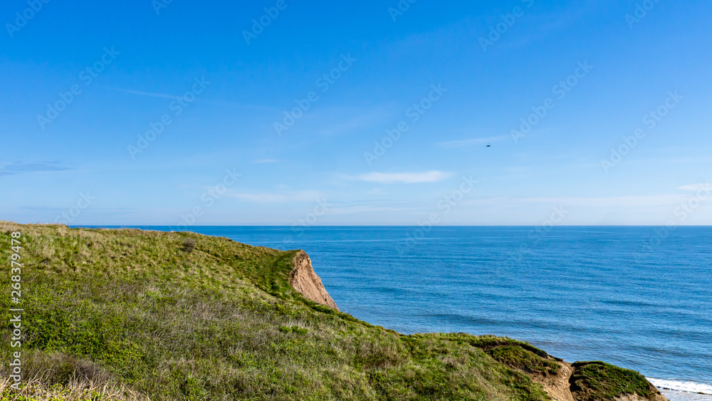 Cliff edge at Seaham Hall Beach in County Durham showing green grass at the edge of a cliff outlooking a calm North Sea.  Image taken on a warm sunny day.