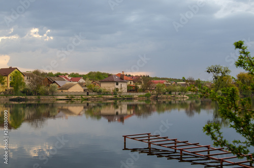 Lake in a village with a reflection of the sky before the rain