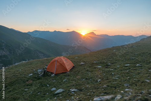 Wide view of orange tent at sunrise with mountain background and sun