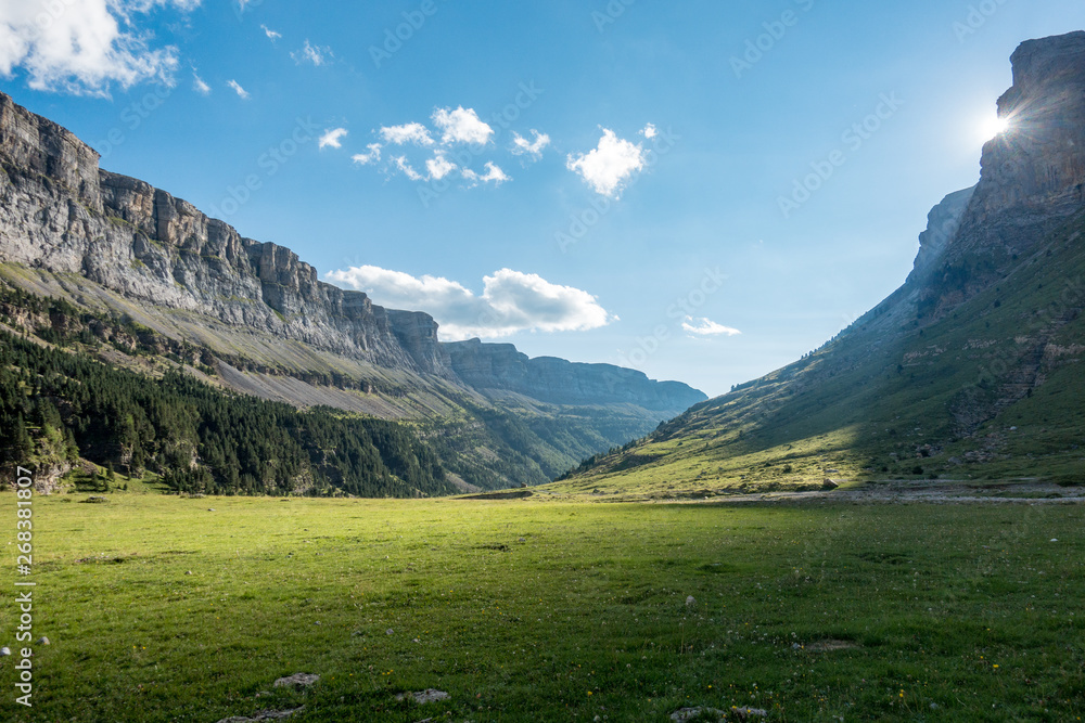 Sun shining over glacier valley with green grass and forests in background