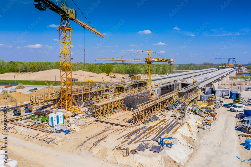 Cranes in the construction of a bridge for a highway. Aerial view
