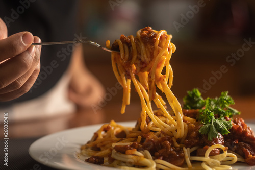 a woman feed herself  a plate of spaghetti served with the beef tomato sauce with ingredients. selective focus