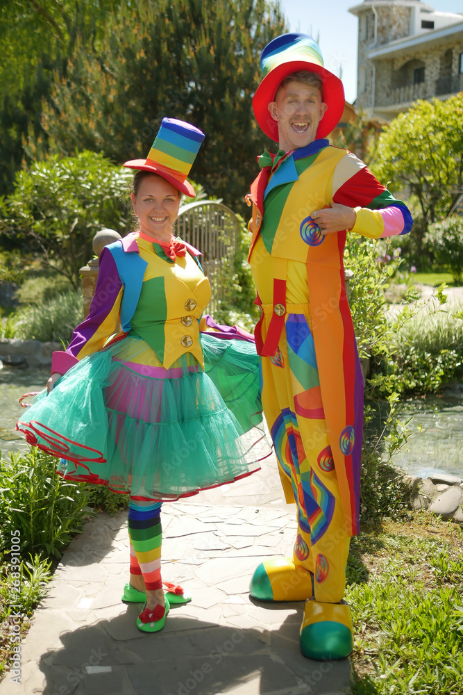 couple of funny clowns, a guy and a girl in a beautiful summer park, on a background of greenery