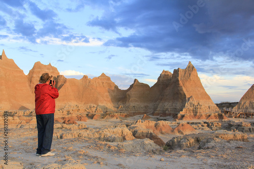 Man in red jacket and cowboy hat taking photographs in Badlands National Park at sunrise