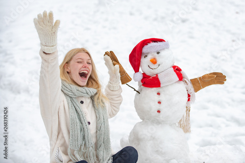 Excited girl plaing with a snowman on a snowy winter walk. Making snowman and winter fun. Cute snowman in hat and scalf on snowy field. photo