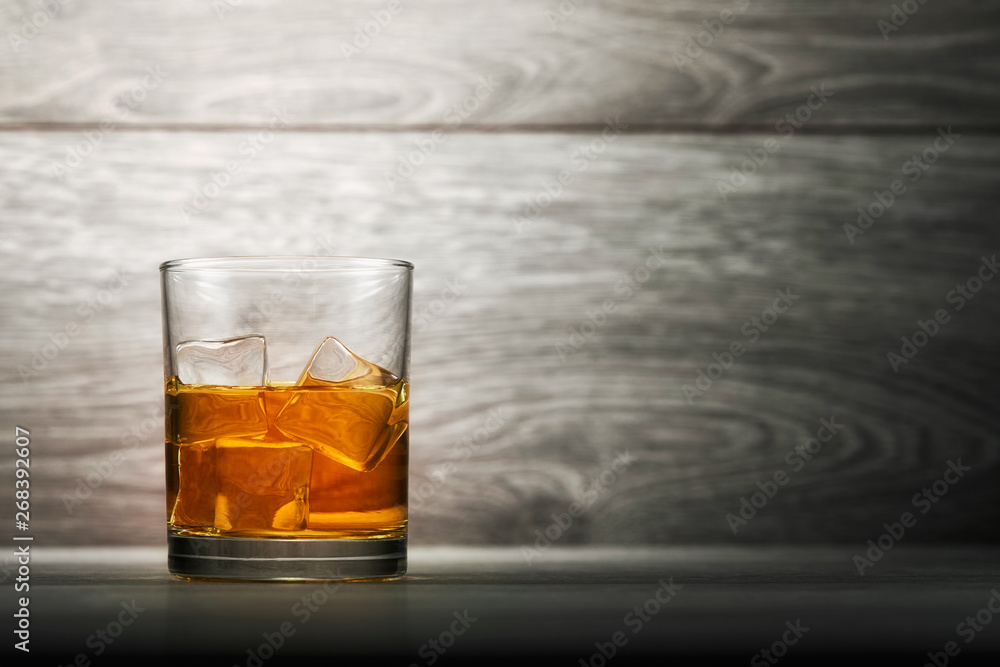 Whiskey glass and ice on wooden bar counter background